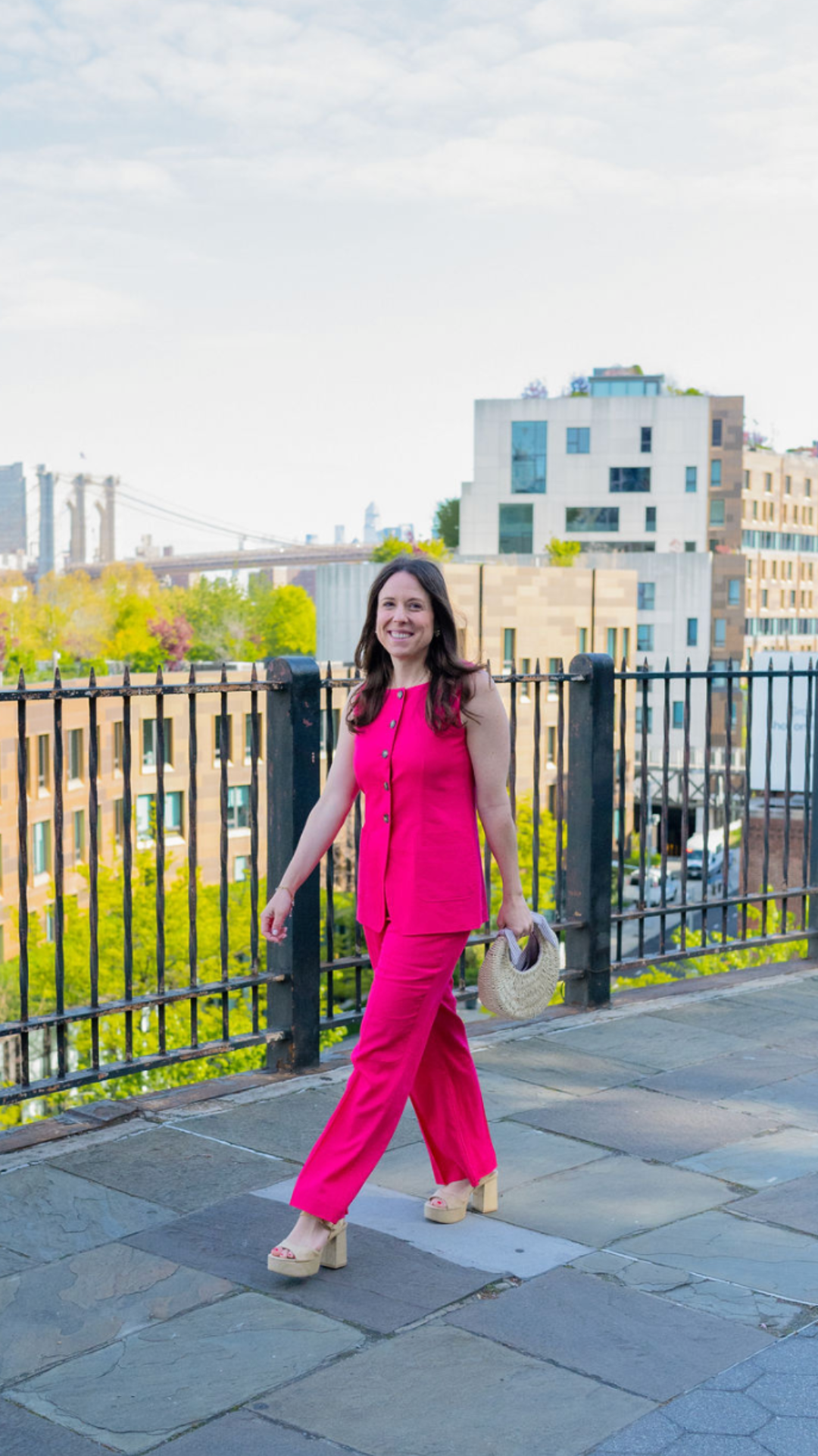Elizabeth in a bright pink suit, walking along a Brooklyn promenade